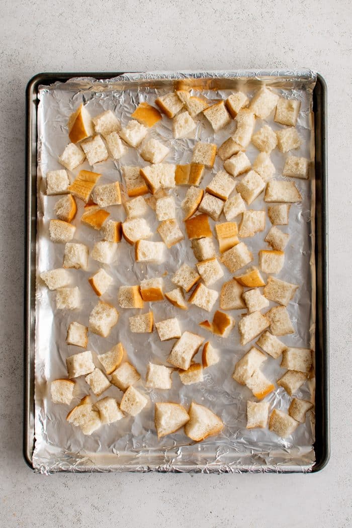 Small cubed bread pieces spread over a large baking sheet lined with aluminum foil.