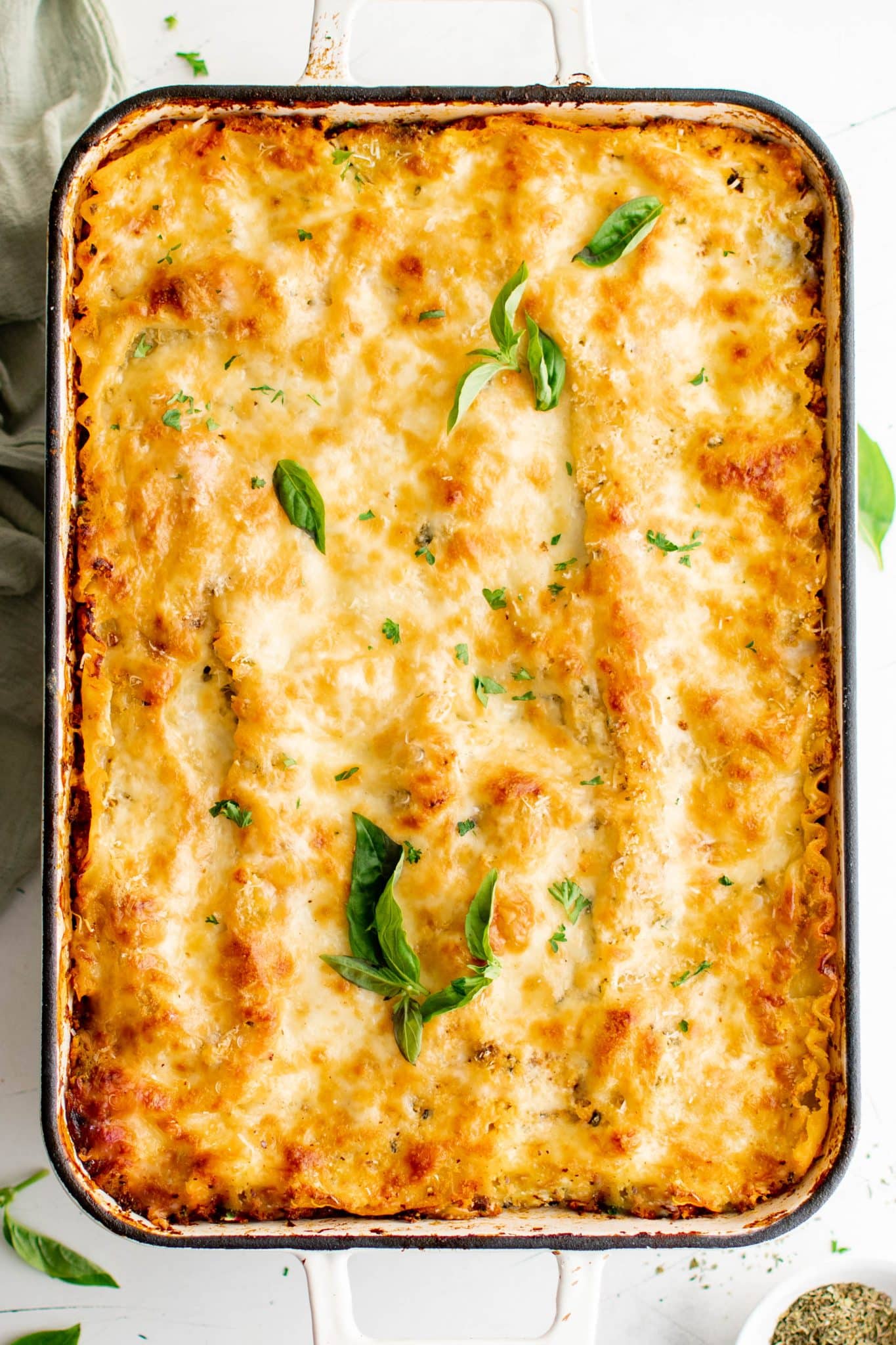 Large 9x13 baking dish filled with cheesy, golden, and bubbly homemade lasagna garnished with fresh basil leaves.