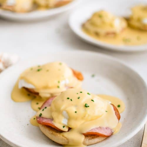 Three white plates each with two eggs benedict with hollandaise sauce.