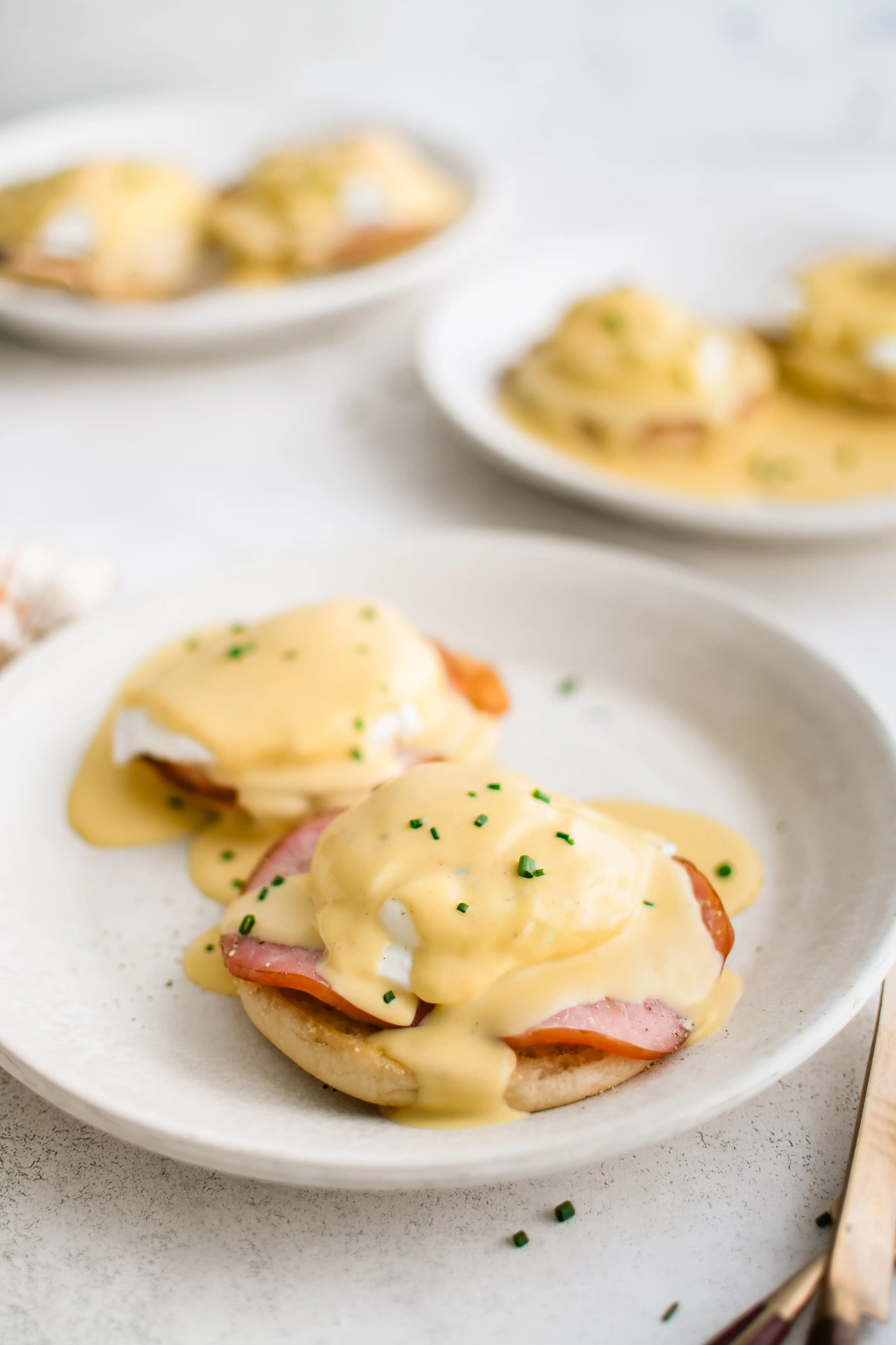 Three white plates each with two eggs benedict with hollandaise sauce.
