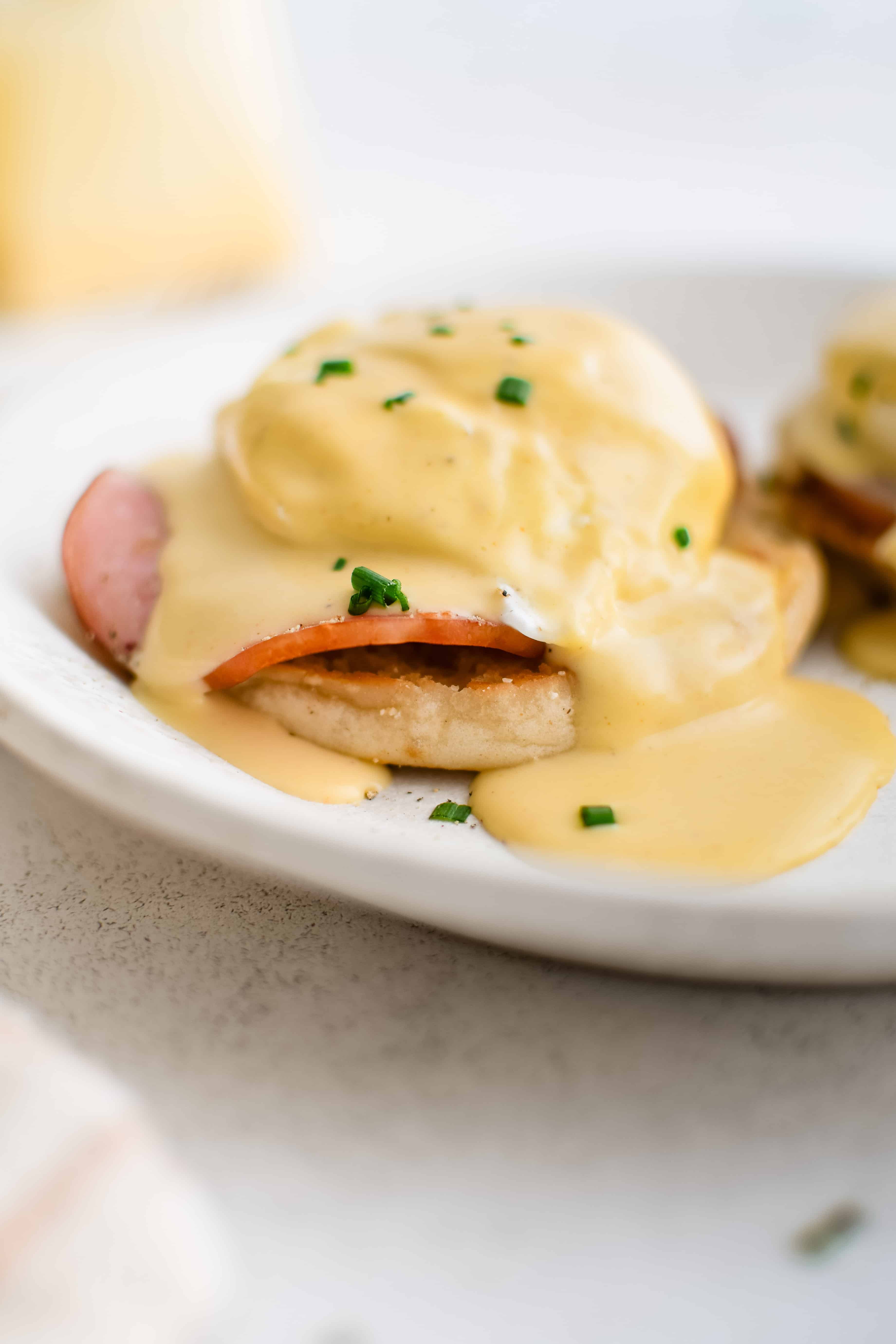 Eggs Benedict with poached egg, Canadian bacon, and hollandaise sauce on an English muffin on a white plate.