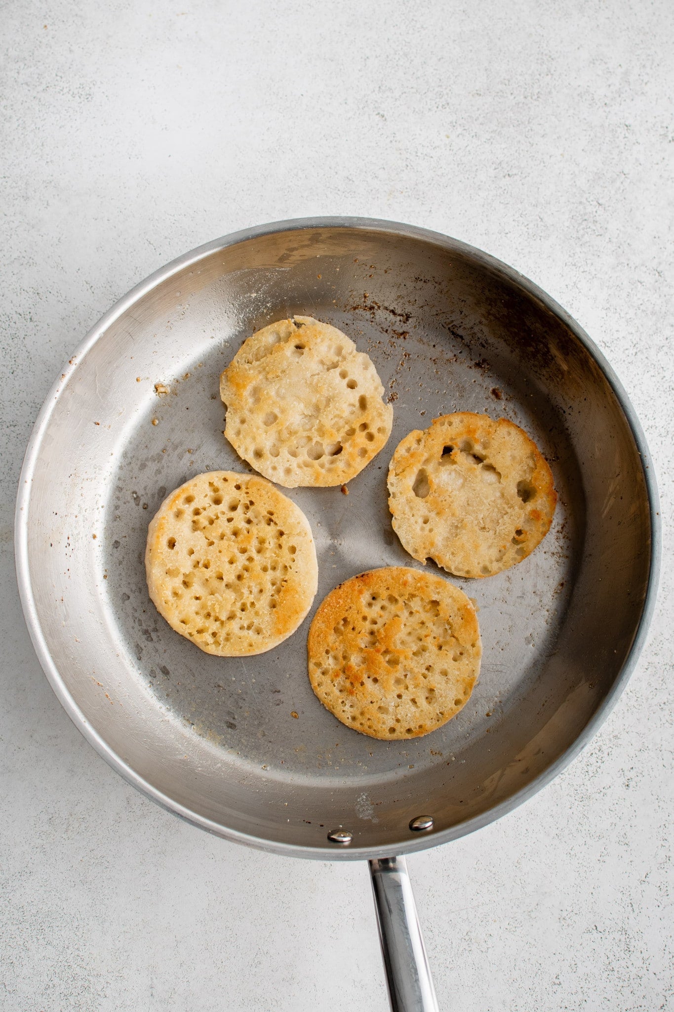 Large skillet filled with four buttery toasted halves of English muffin.