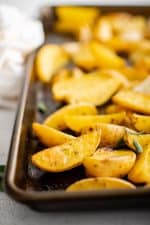 Golden roasted Greek potato wedges seasoned with fresh parsley and oregano, lemon juice, and garlic, on a baking sheet.