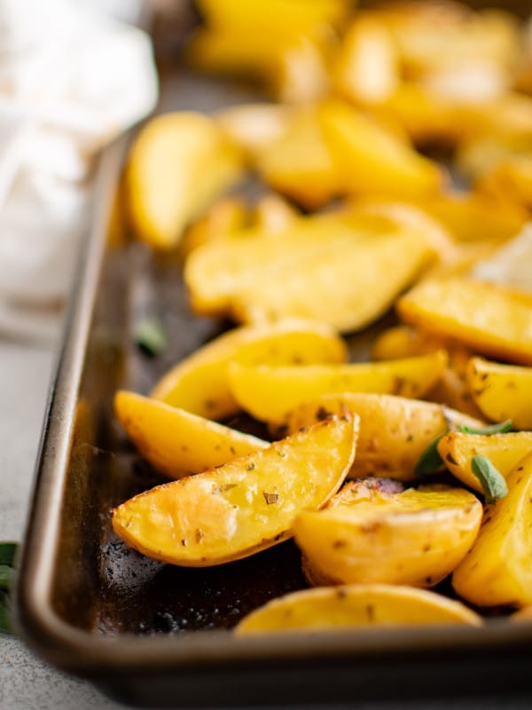 Golden roasted Greek potato wedges seasoned with fresh parsley and oregano, lemon juice, and garlic, on a baking sheet.