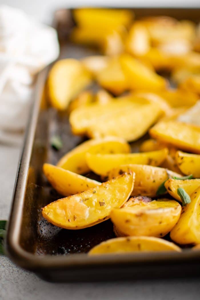 Golden roasted Greek potato wedges seasoned with fresh parsley and oregano, lemon juice, and garlic, on a baking sheet.