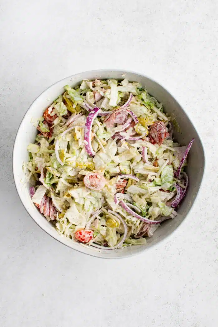 Large bowl filled with tossed together Grinder salad coated in creamy, savory, tangy homemade dressing.