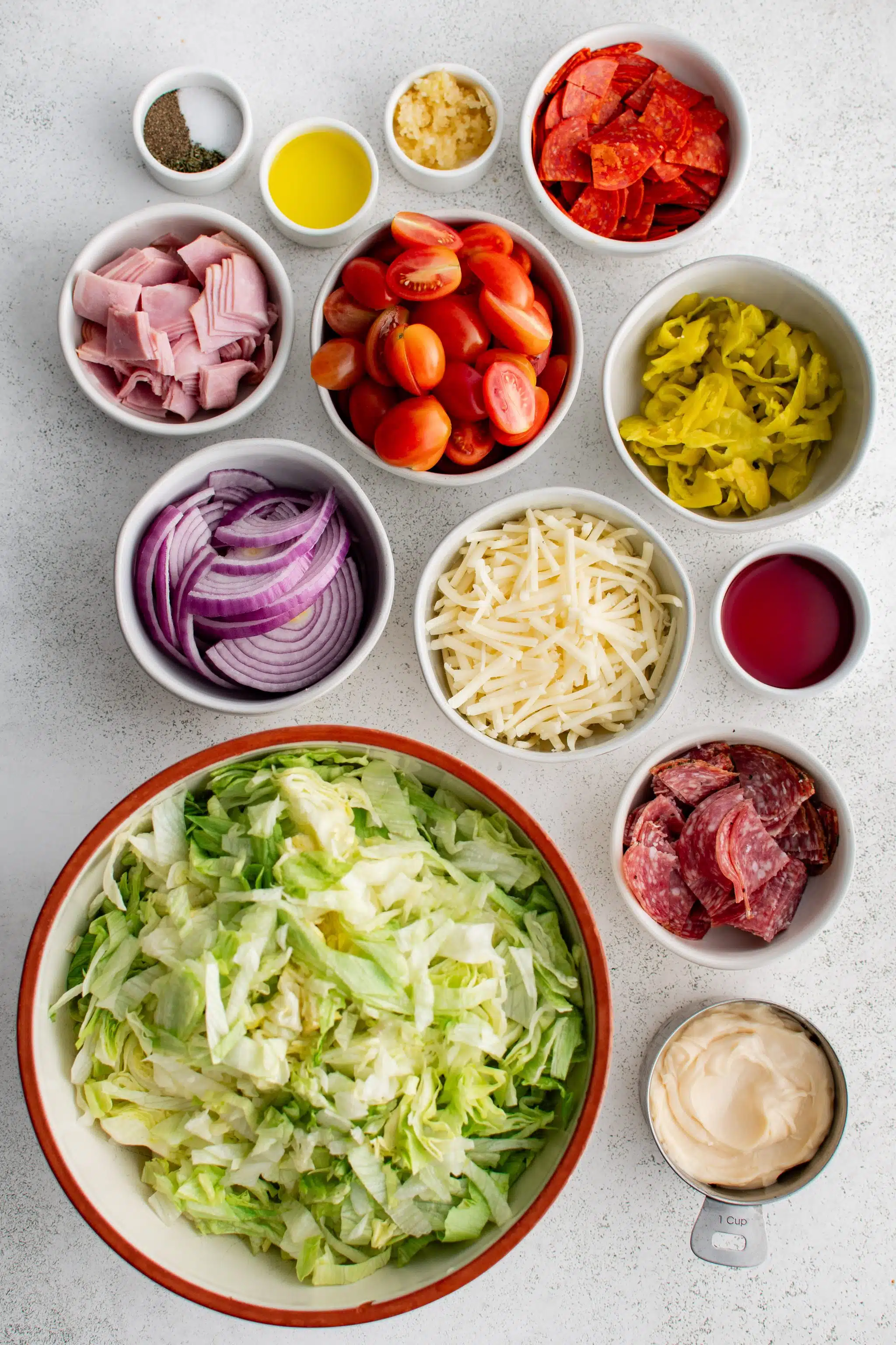 All of the ingredients for Grinder Salad presented in individual measuring cups and ramekins.