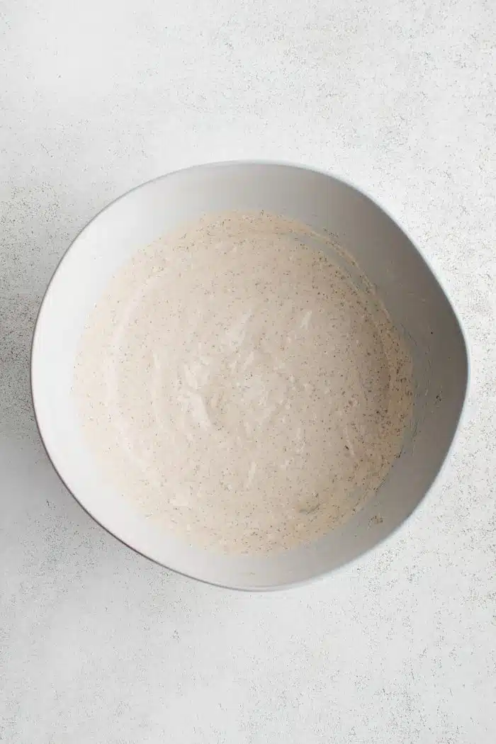 Ceramic mixing bowl filled with whisked together creamy homemade dressing for grinder salad.