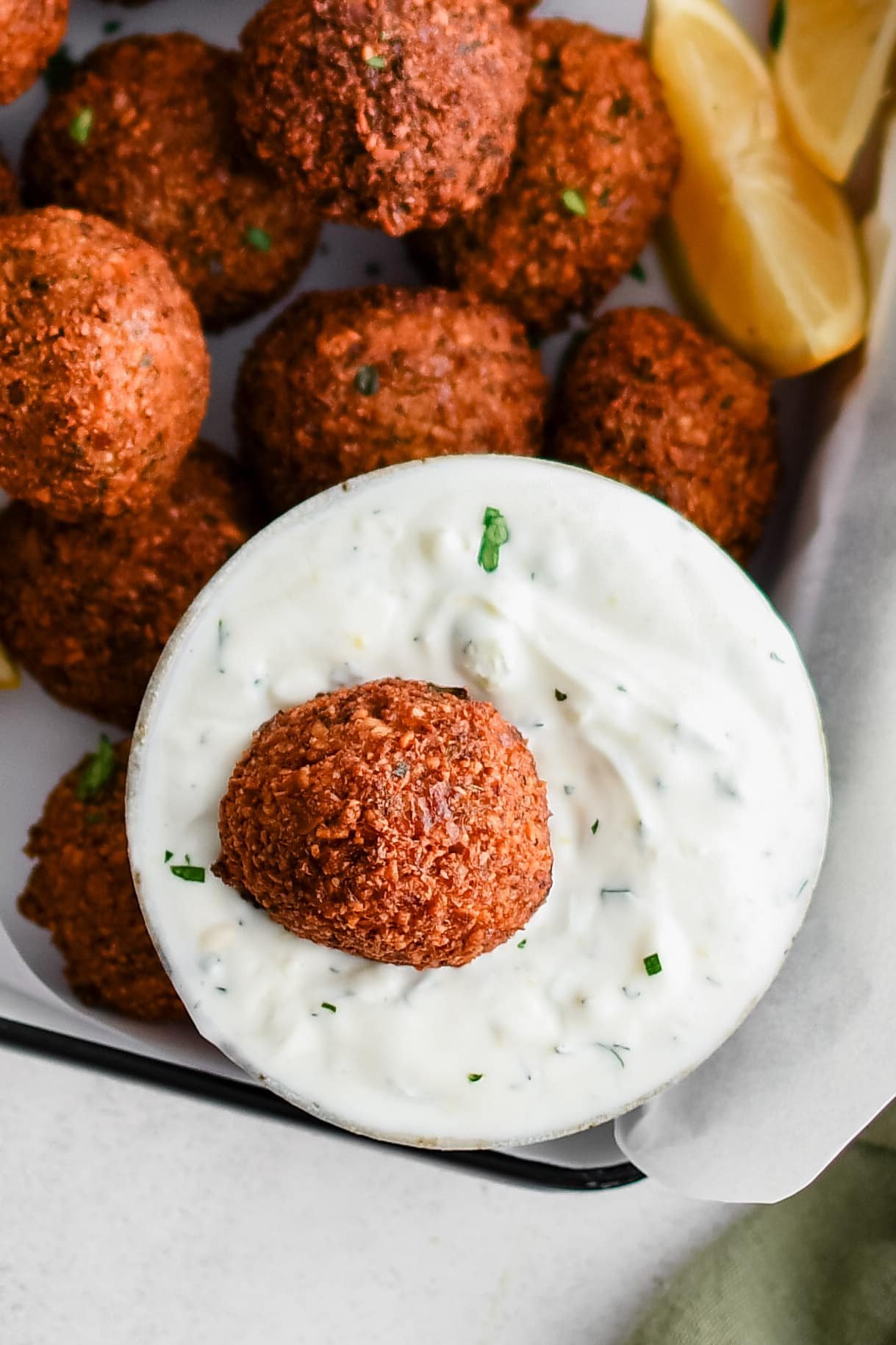 Single fried homemade falafel ball in a small bowl filled with tzatziki.