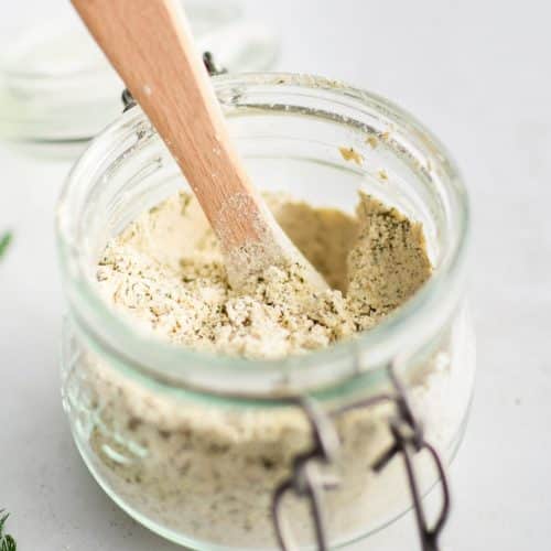 Small glass jar filled with homemade ranch seasoning mix with a small wooden measuring spoon.