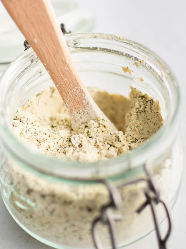 Small glass jar filled with homemade ranch seasoning mix with a small wooden measuring spoon.