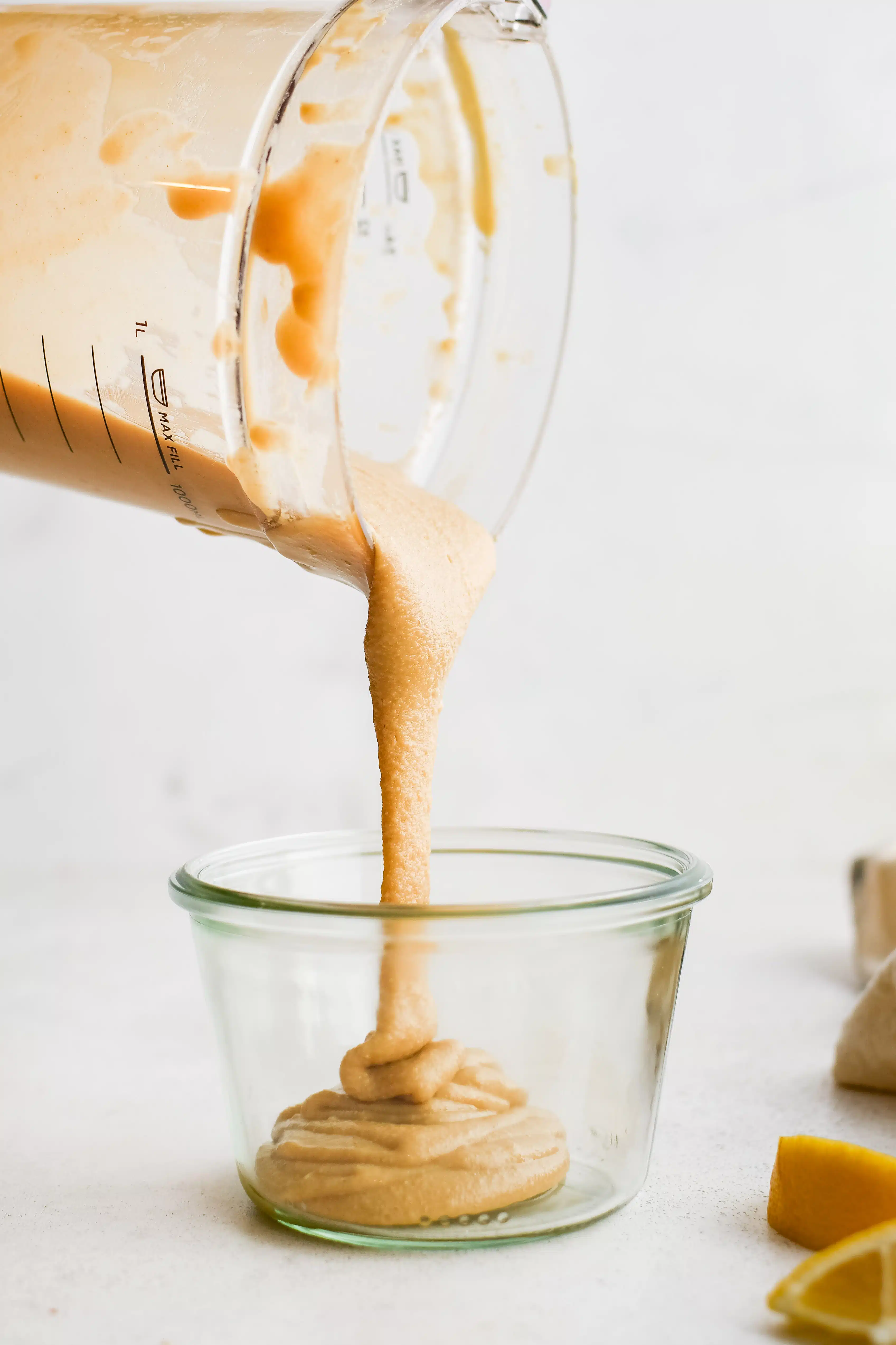 Homemade tahini being poured out of a large blender into a smaller glass container.