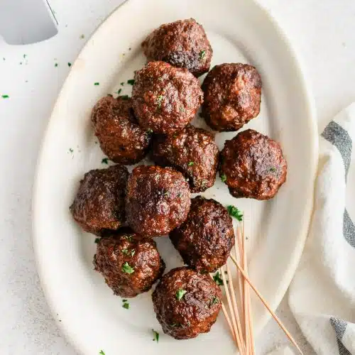 Oval plate with air fryer meatballs garnished with minced parsley and served with a small pile of toothpicks for serving.