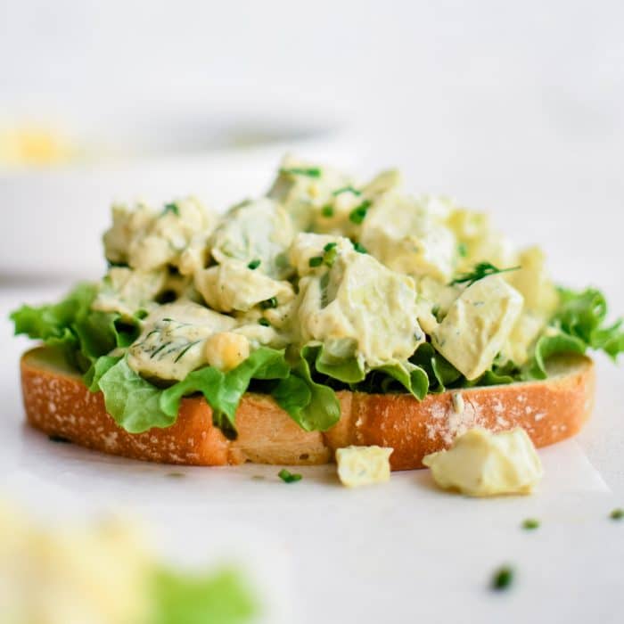 Toasted white bread topped with crisp lettuce and creamy avocado egg salad and garnished with fresh chives.