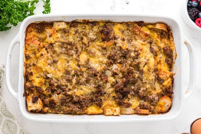 Freshly baked breakfast casserole in a white dish with golden brown bread, melted cheese, and browned sausage on top.