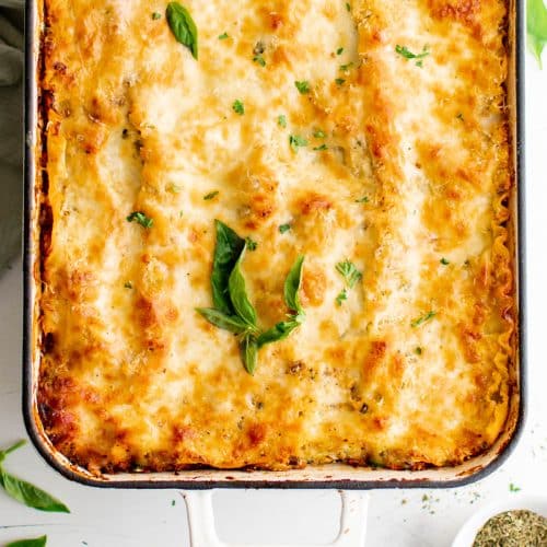 Large 9x13 baking dish filled with cheesy, golden, and bubbly homemade lasagna garnished with fresh basil leaves.