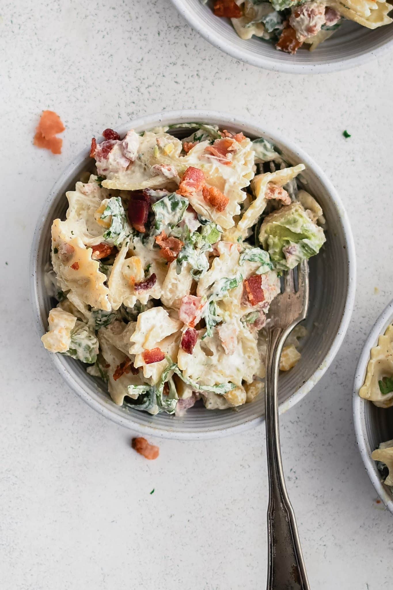 Small serving bowl filled with creamy BLT pasta salad made with bowtie pasta, arugula, avocado, tomato, bacon, and corn in a creamy mayo and sour cream dressing.
