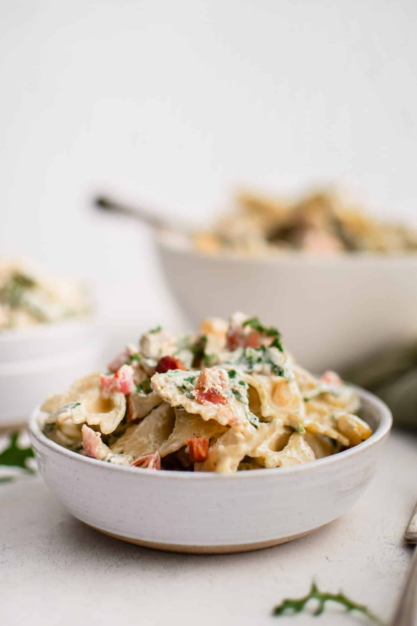 Small serving bowl filled with creamy BLT pasta salad made with bowtie pasta, arugula, avocado, tomato, bacon, and corn in a creamy mayo and sour cream dressing.