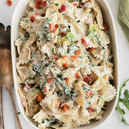 Large oval serving plate filled with creamy BLT pasta salad made with bowtie pasta, arugula, avocado, tomato, bacon, and corn in a creamy mayo and sour cream dressing.