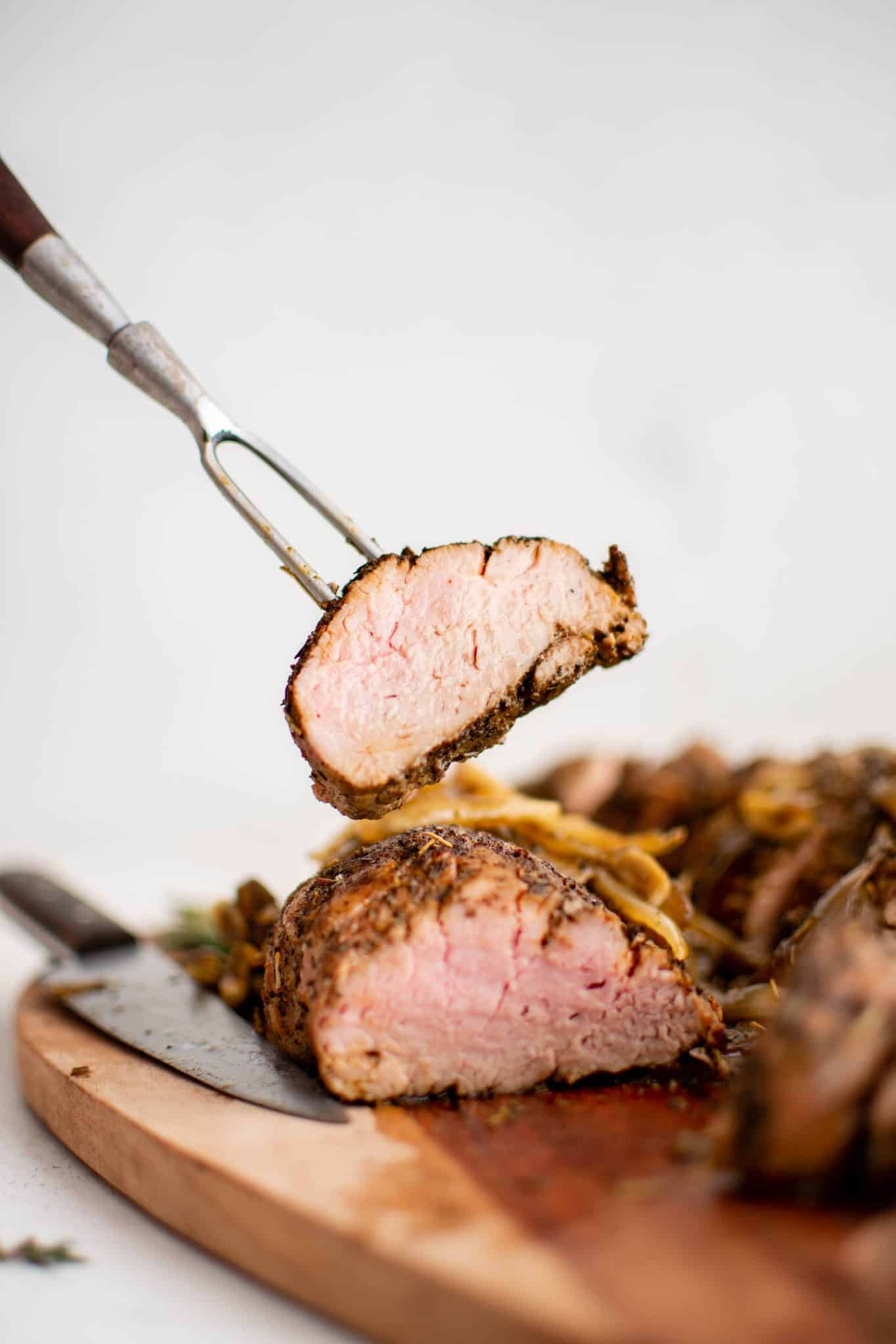 Meat fork holding a single pork medallion showing its juicy interior and herb seasoned exterior.