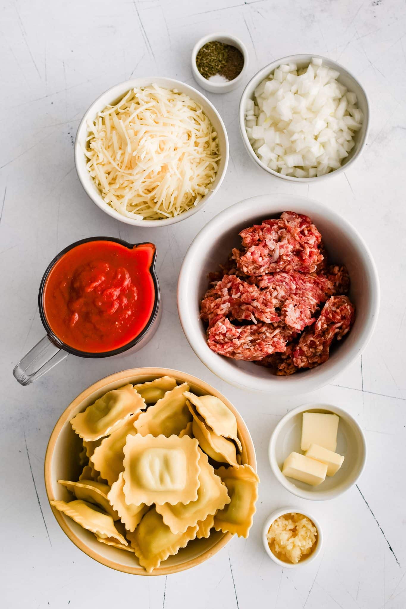 All of the ingredients for baked ravioli presented in individual measuring cups and ramekins.