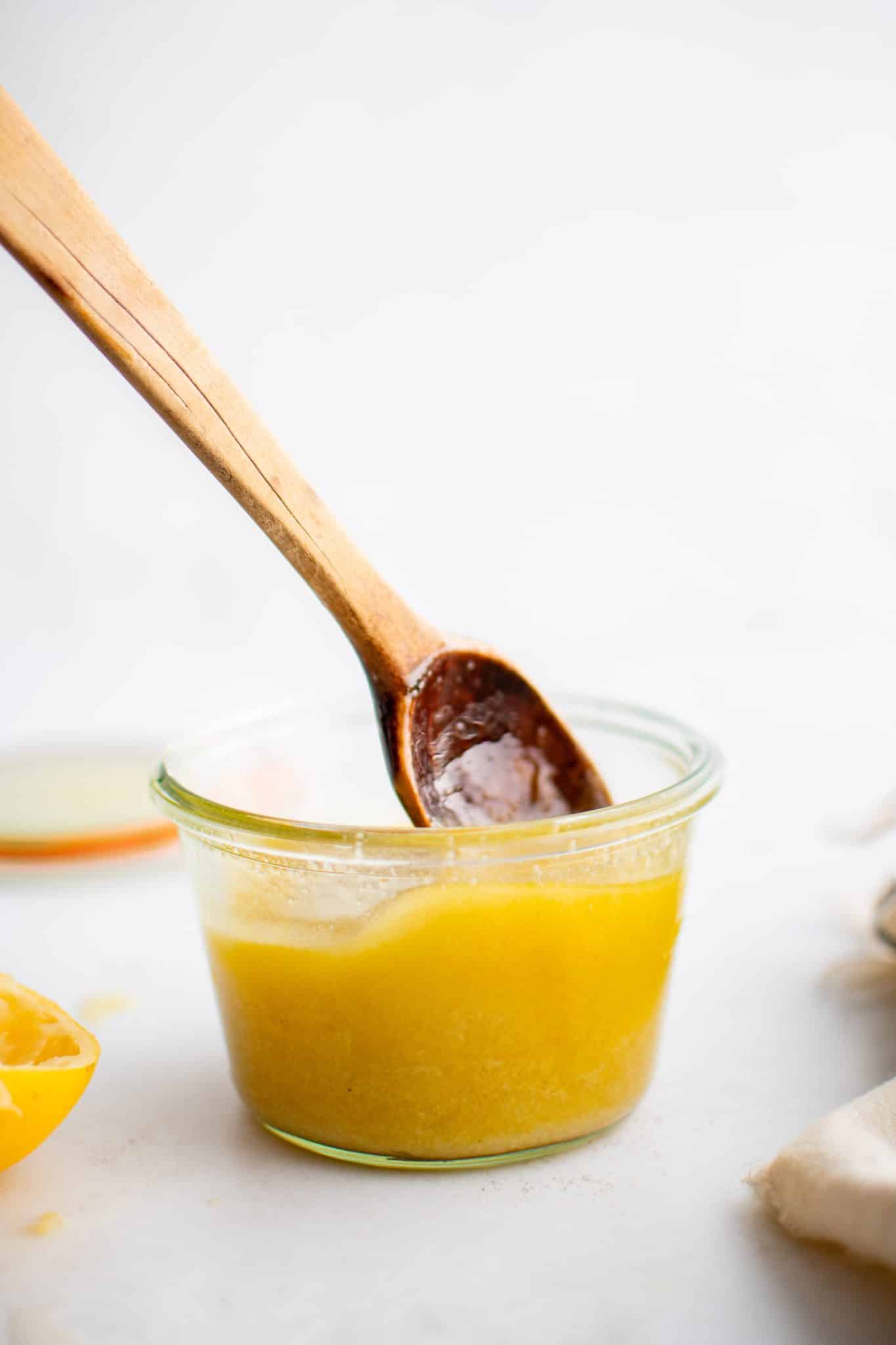 Small wooden spoon in a glass jar filled with golden yellow champagne vinaigrette.