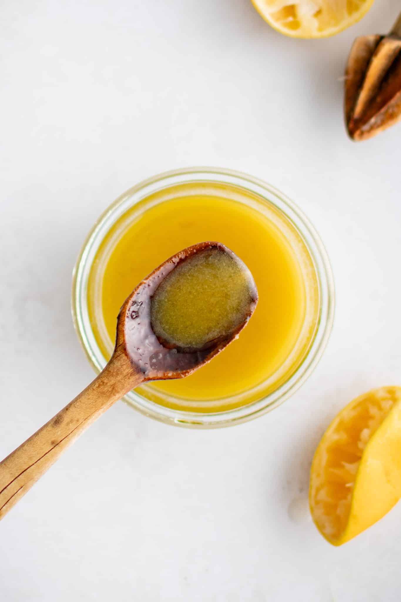 Small wooden spoon in a glass jar filled with golden yellow champagne vinaigrette.