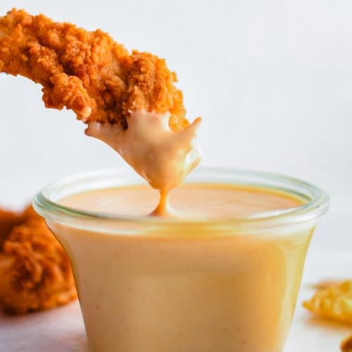 Crispy chicken tender being dipped into a small glass jar filled with homemade Homemade Chick Fil A Sauce.