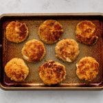 Eight crab cakes on a large baking sheet sprayed with non-stick cooking spray.