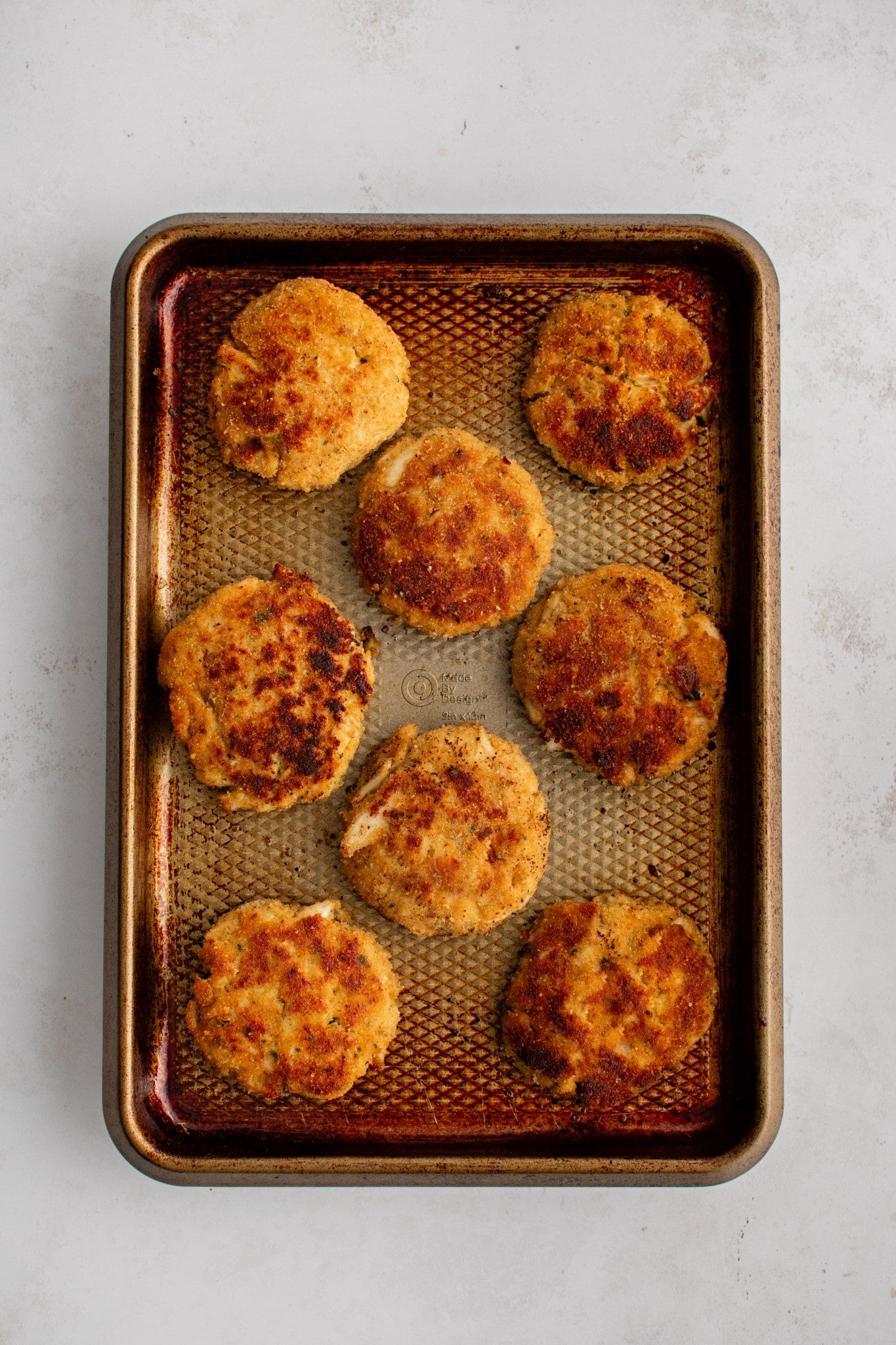 Eight crab cakes on a large baking sheet sprayed with non-stick cooking spray.