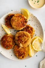 Speckled white plated presented with six golden baked crab cakes served with fresh lemon wedges and garnished with freshly minced parsley.
