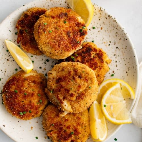 Speckled white plated presented with six golden baked crab cakes served with fresh lemon wedges and garnished with freshly minced parsley.