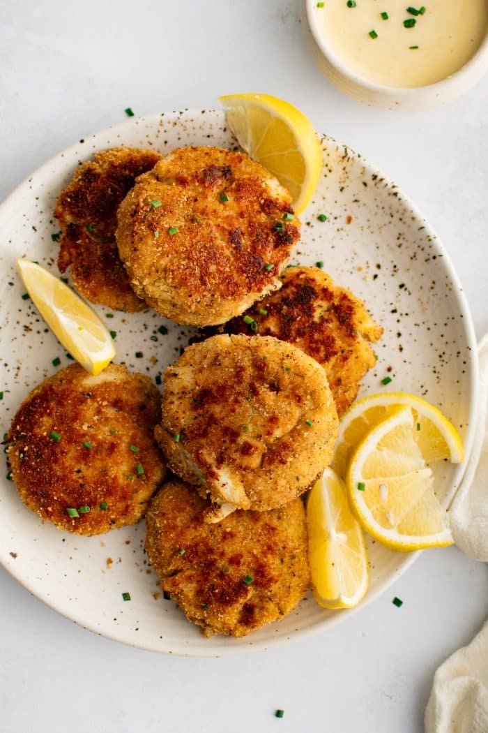 Speckled white plated presented with six golden baked crab cakes served with fresh lemon wedges and garnished with freshly minced parsley.