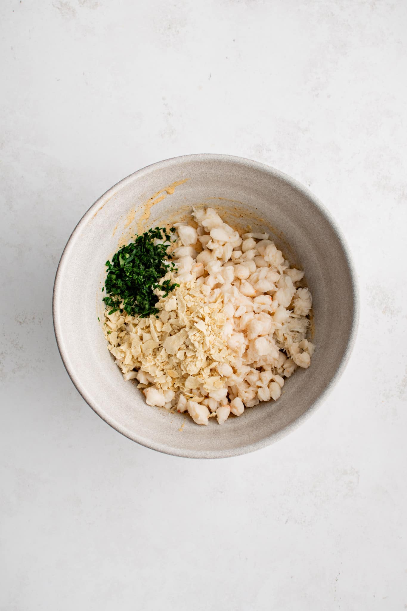 Lump crabmeat, crackers, and parsley added to the large bowl filled with Whisked together mayonnaise, egg, mustard, old bay seasoning, lemon zest, Worcestershire sauce, and salt.
