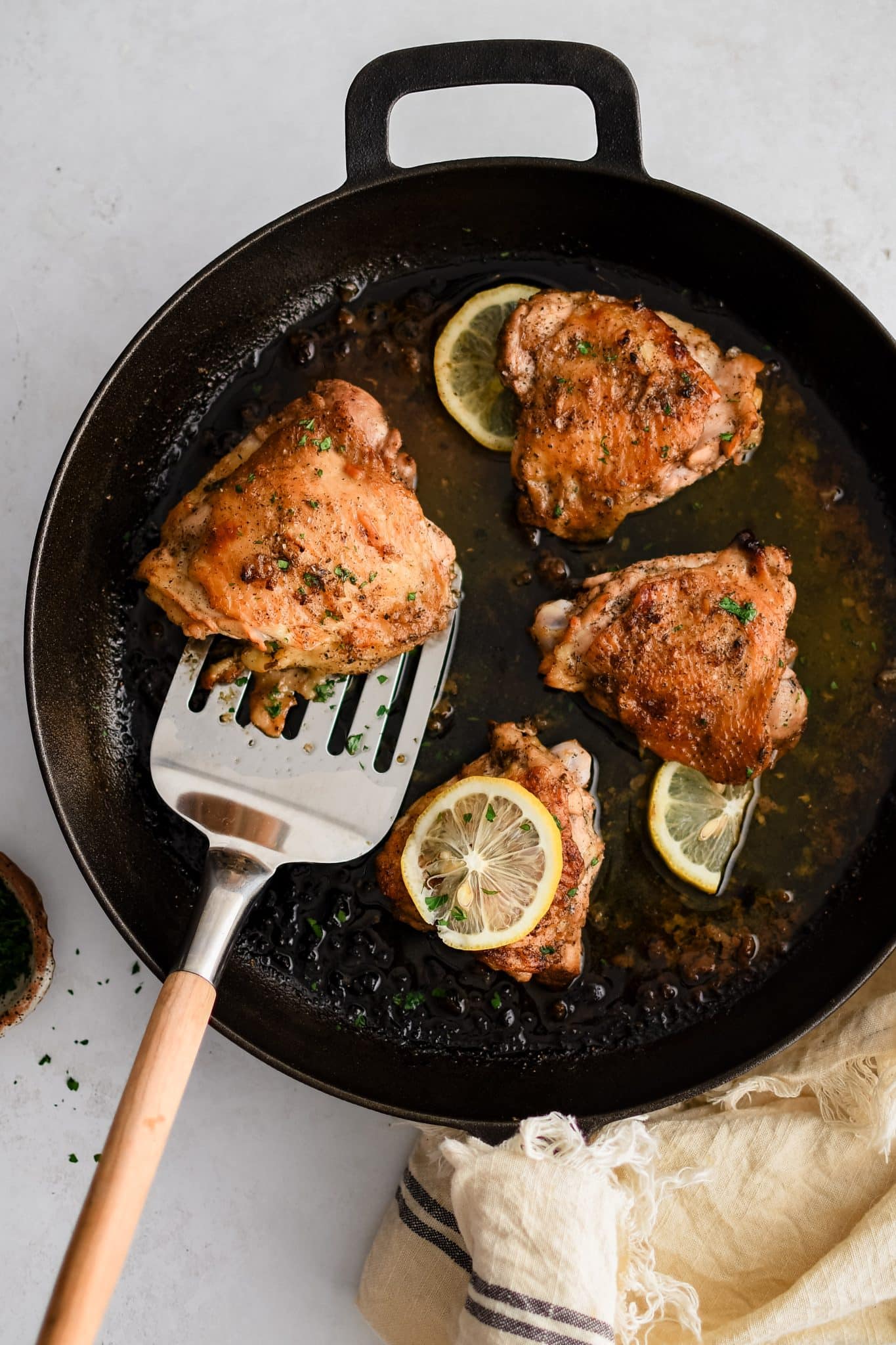 Four fully cooked Greek lemon chicken thighs with golden crispy skin and juicy meat resting in a large cast iron skillet with fresh sliced lemons.