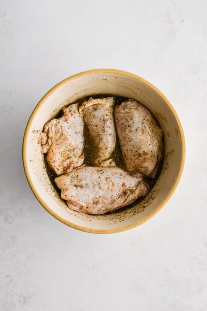 Four bone-in skin on chicken thighs in a medium bowl marinating in a Greek inspired lemon marinade made with lemon juice, olive oil, fresh garlic, dried oregano, salt, and black pepper.