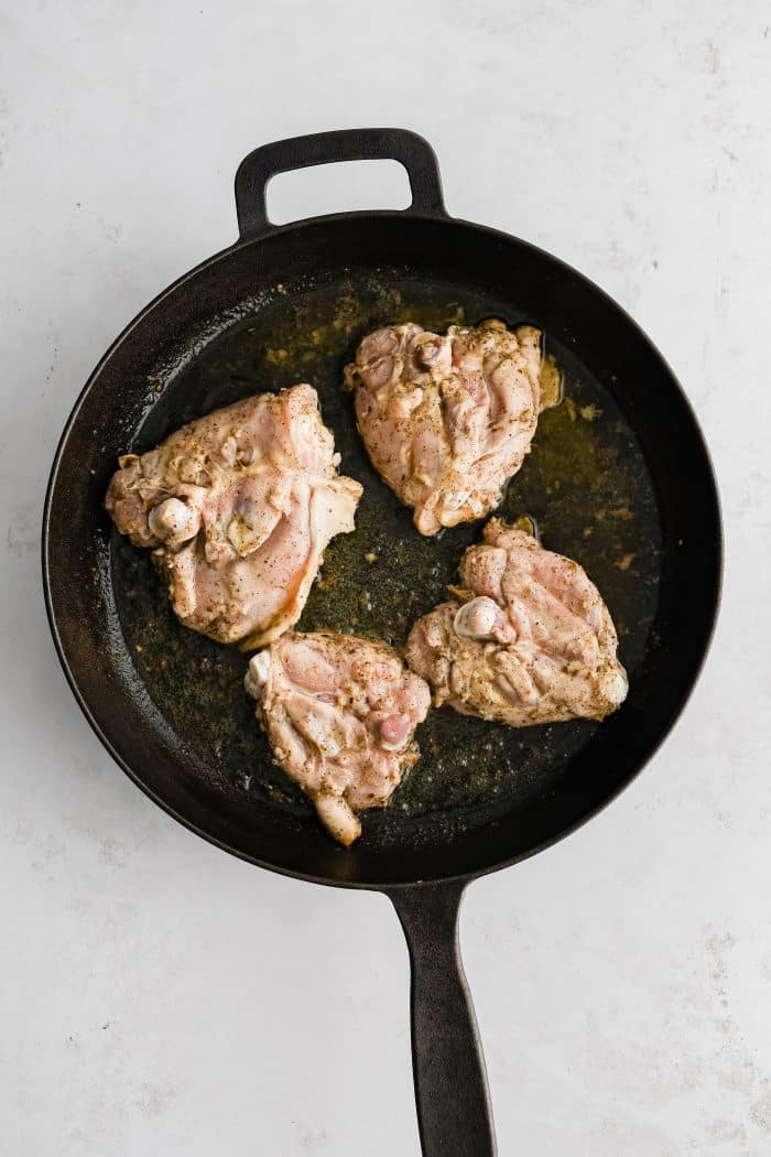Four bone-in skin-on marinated chicken thighs placed in a large cast-iron skillet skin-side-down.