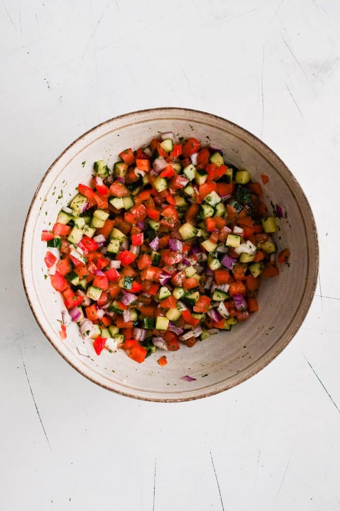 Large mixing bowl filled with chopped cucumbers, tomatoes, red bell peppers, and red onions in a lemon vinaigrette.