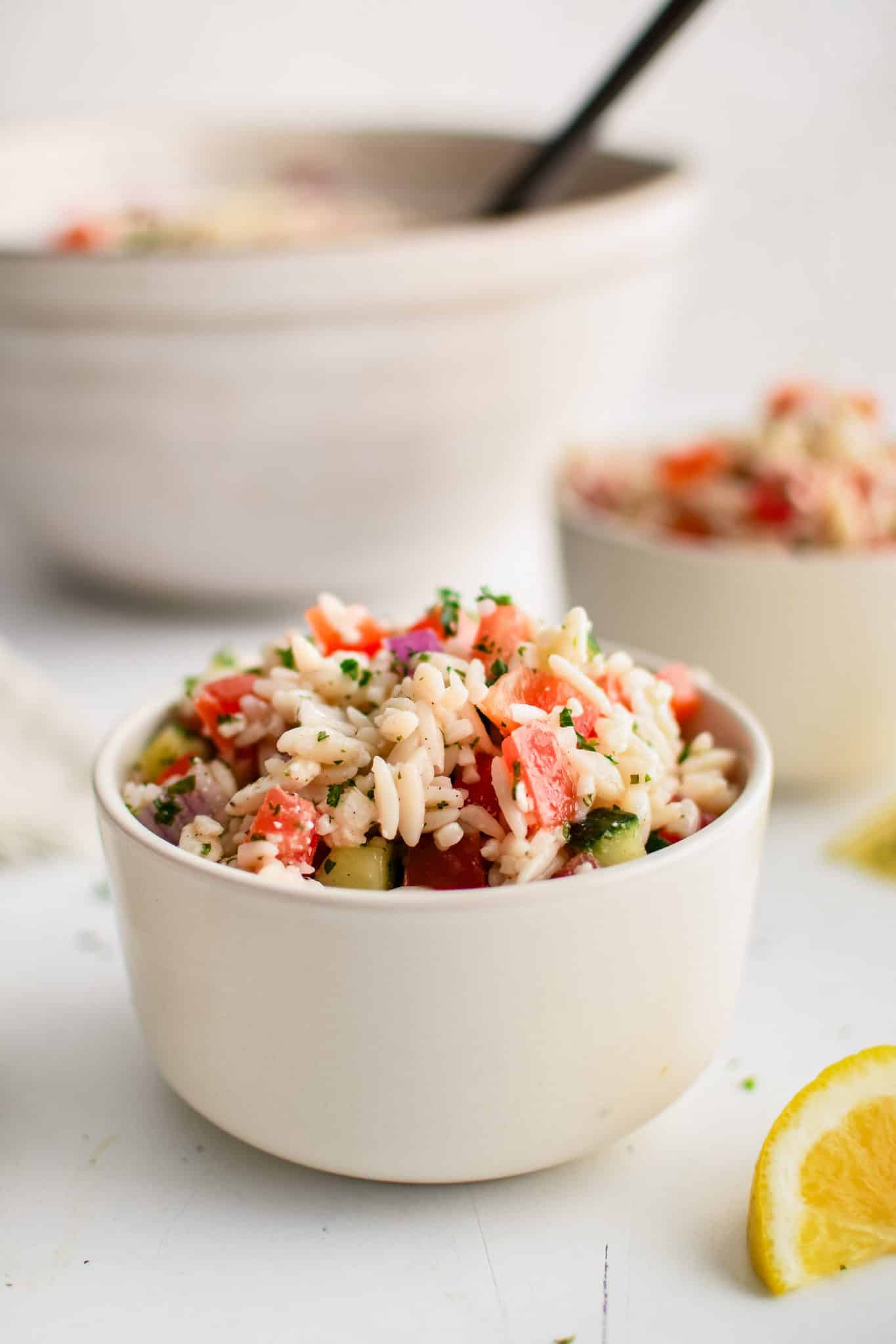 Small serving bowl filled with Mediterranean orzo salad made with cooked orzo, red onion, bell pepper, cucumber, and tomatoes in a lemon vinaigrette. 