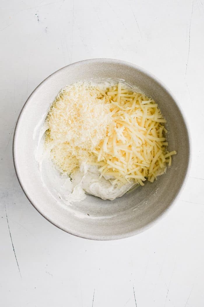 White mixing bowl filled with cream cheese mixture, shredded mozzarella cheese, and parmesan cheese.