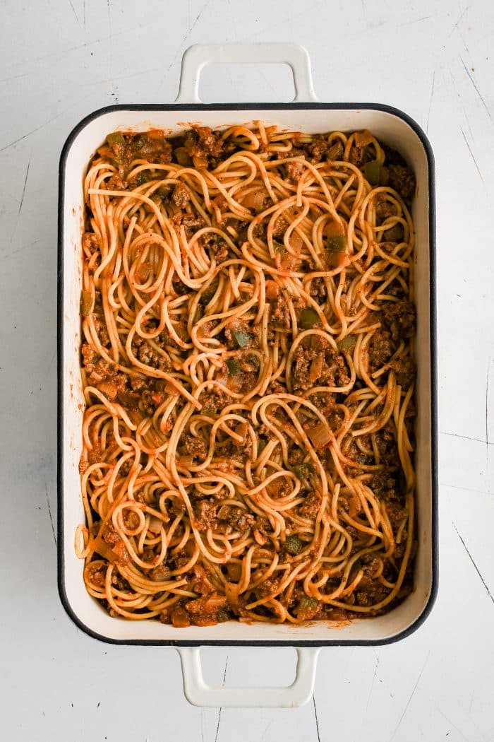 Large 9x13-inch casserole pan filled with al dente spaghetti noodles mixed in meat and tomato sauce.