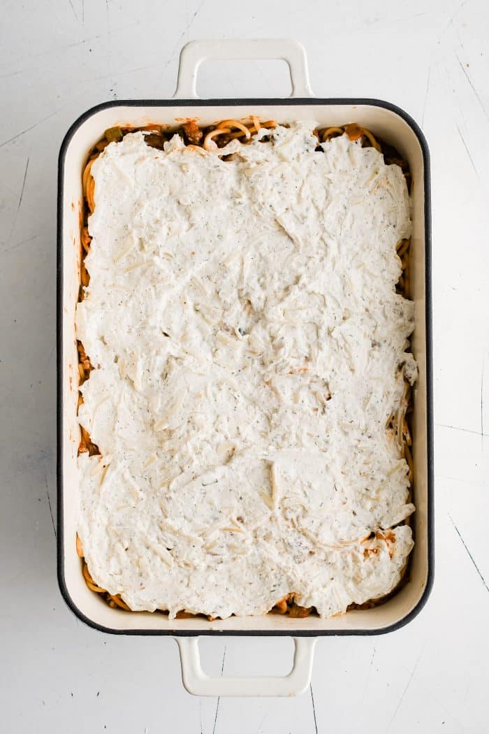 Large 9x13-inch casserole pan filled with al dente spaghetti noodles mixed in meat and tomato sauce and topped with a thick layer of cream cheese mixture.