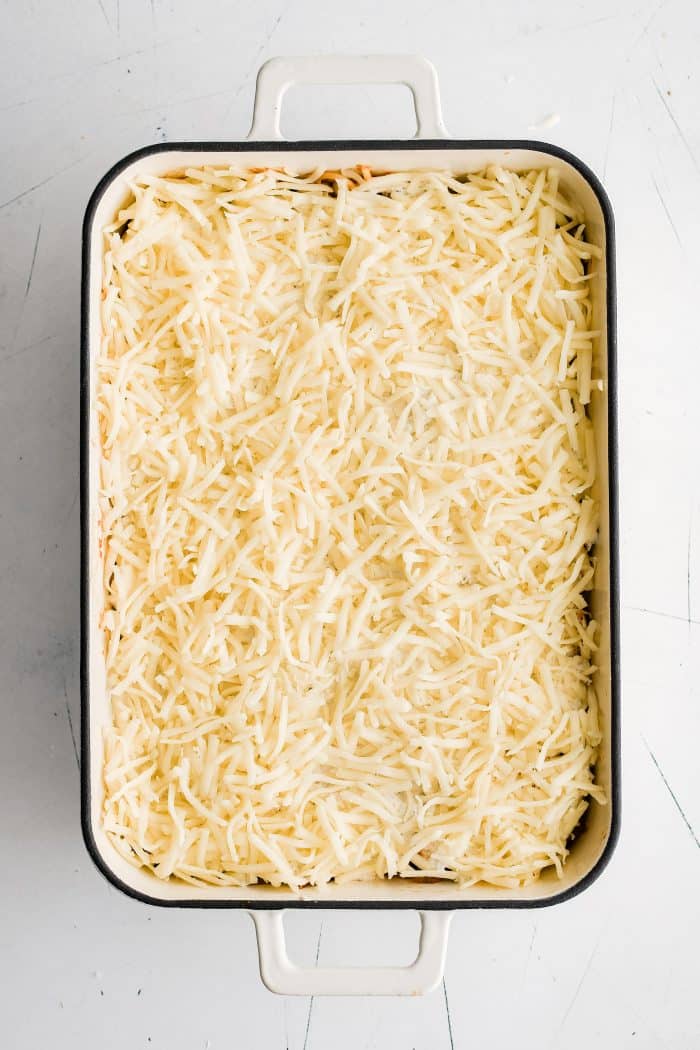 Large 9x13-inch casserole pan filled with al dente spaghetti noodles mixed in meat and tomato sauce, topped with a thick layer of cream cheese mixture, and topped with shredded mozzarella cheese.