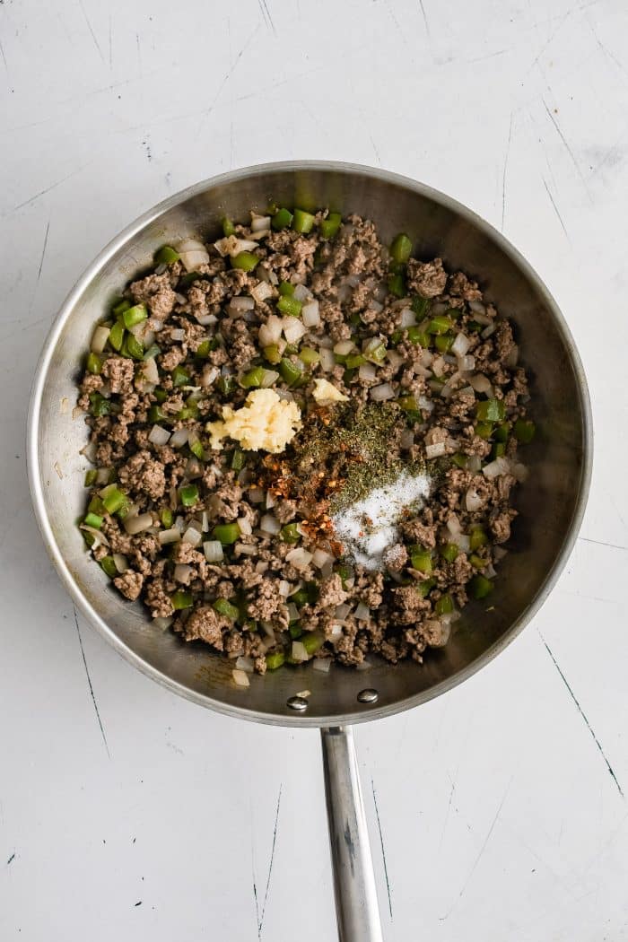 Browned ground beef with softened onions and diced green onions in a large stainless steel skillet.