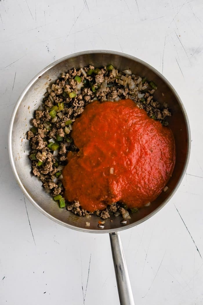Tomato pasta sauce added to seasoned ground beef and veggies in a large stainless steel skillet.