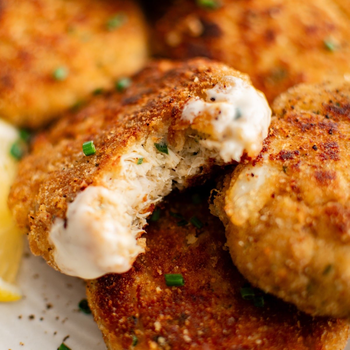 Speckled white plate presented with golden baked crab cakes with the one center focus crab cake with a bite take out.