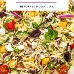 Pinterest pin image for Mediterranean orzo salad with a close-up background of orzo pasta, cucumber, cherry tomatoes, yellow bell pepper, red onion, Kalamata olives, feta cheese, parsley, mint, and black pepper, topped with a white text box that reads โMEDITERRANEAN ORZO SALADโ and โTHEFORKEDSPOON.COM.โ
