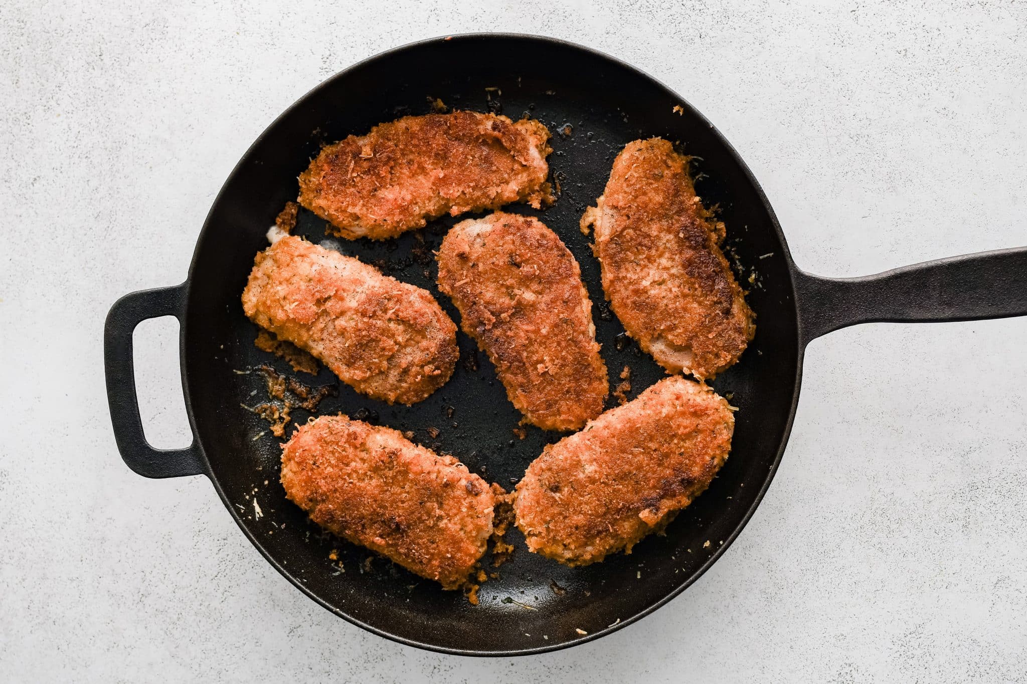 Cast iron skillet filled with Parmesan crusted pork chops that are deeply golden and crisp on both sides.