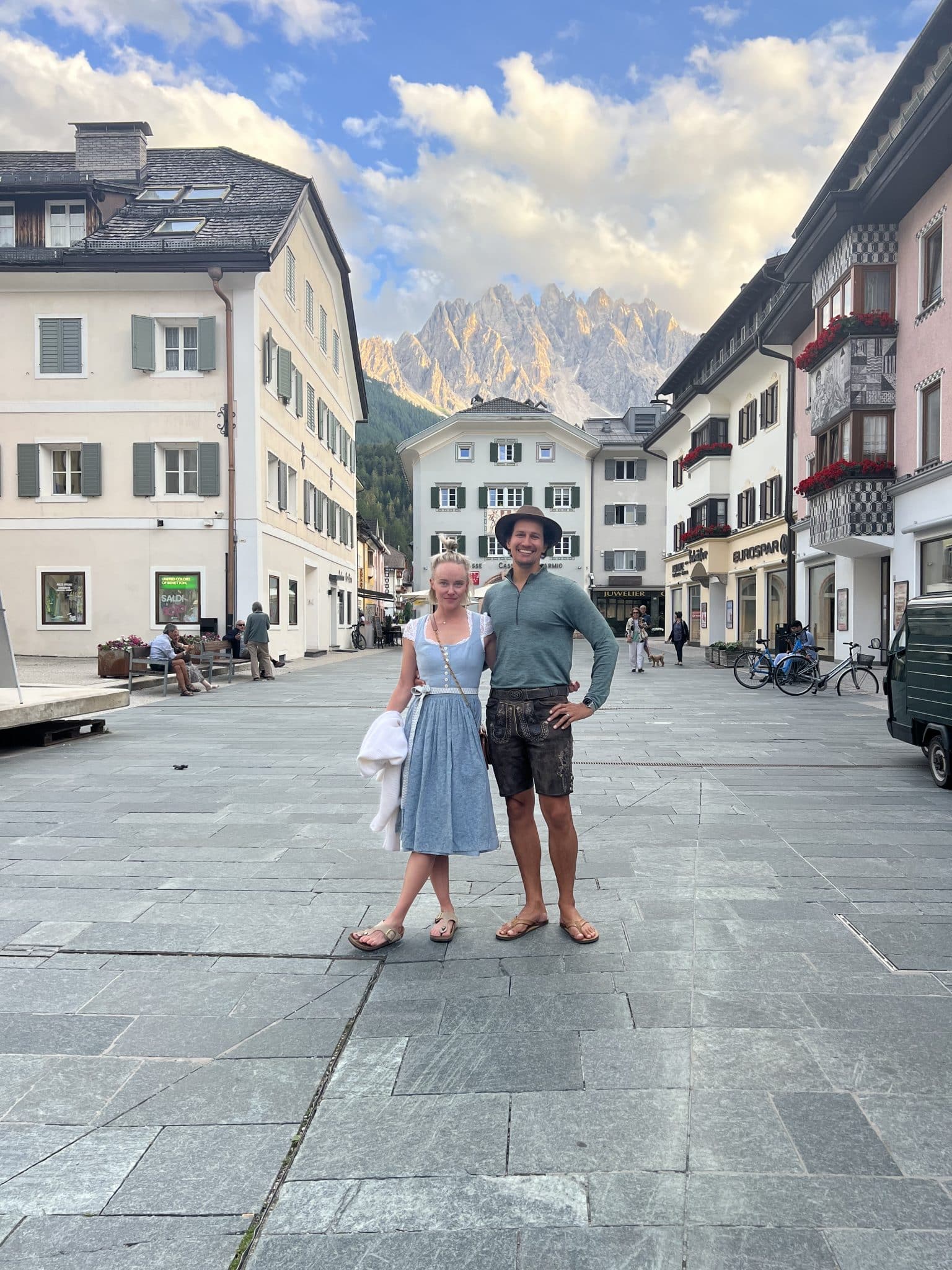 Chef Jessica and Aaron Randhawa dressed in local German clothing in central San Candido Italy with Dolomites in the background.