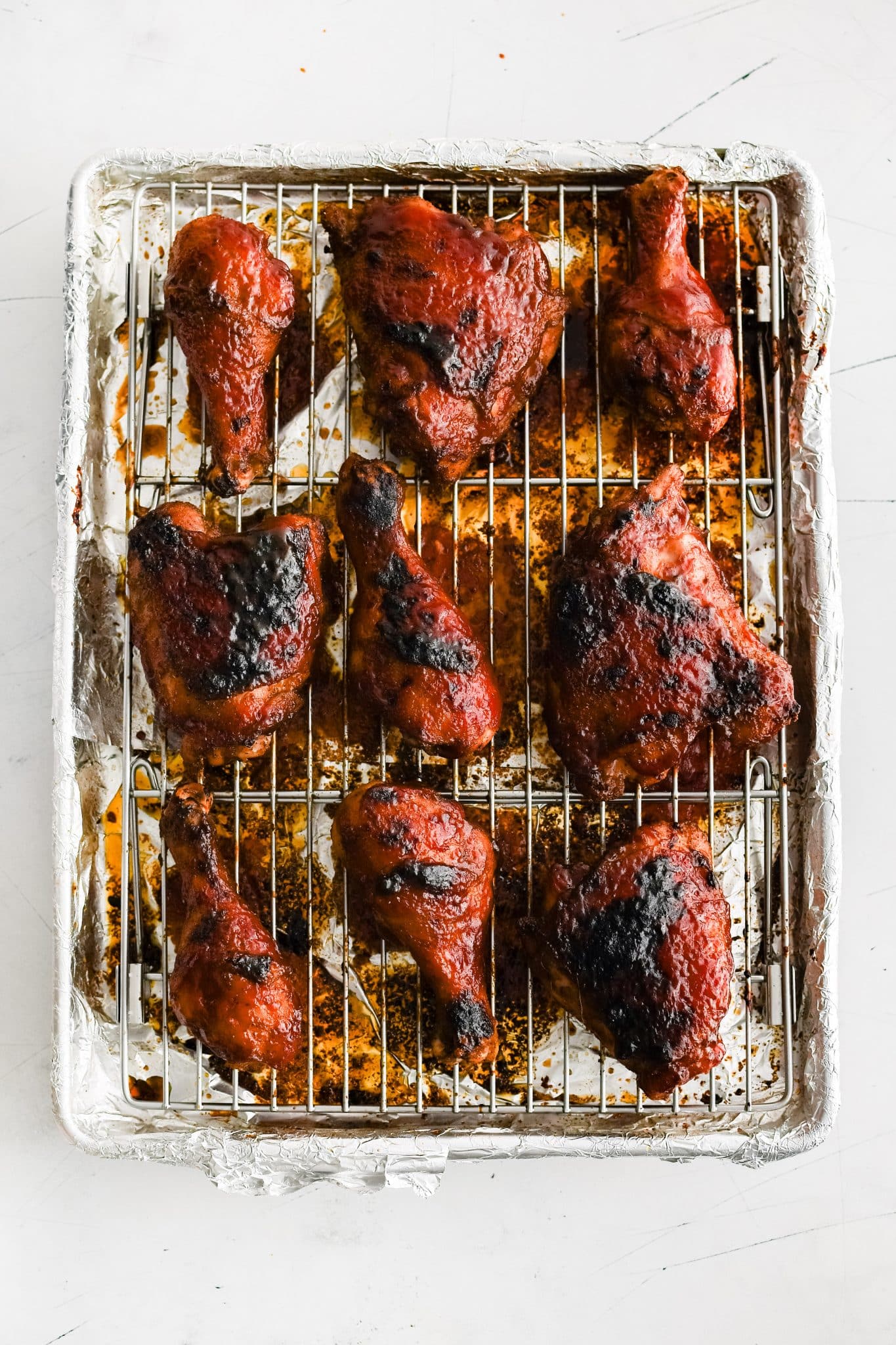 Cooling rack topped with perfectly baked bone-in skin-on BBQ chicken thighs and drumsticks coated in sticky BBQ sauce.